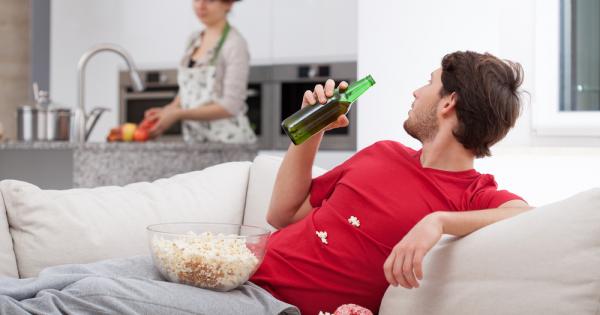 Мъж седи на дивана и гледа телевизия Неговата партньорка приготвя